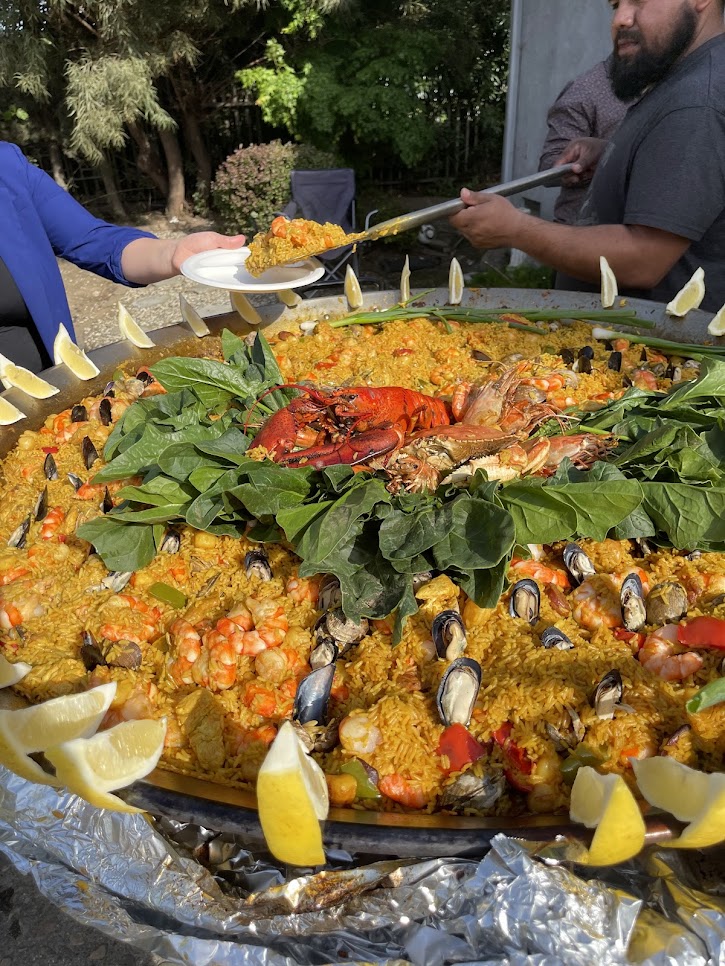 Guests being served a large seafood paella outdoors